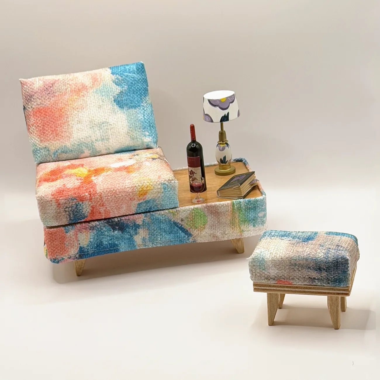 The Waterlily Lounge Set, a miniature seat with angled backrest and wood-top side table in watercolor-style upholstery of turquoise, coral, blush, and cream, with a matching ottoman.